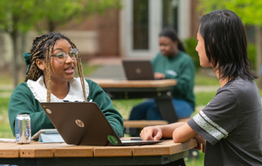 two students sitting at a table with laptop, outdoors